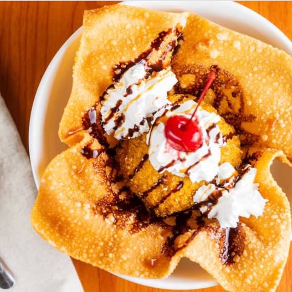 Fried ice cream dessert with whipped cream, chocolate syrup, and a cherry in a crispy shell.