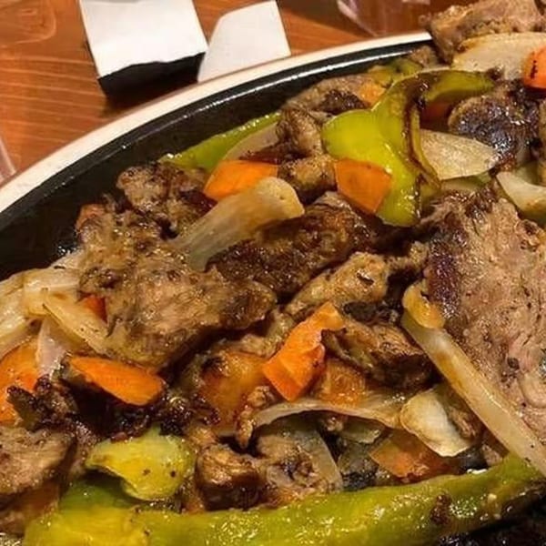 Sizzling fajita meat with green peppers, onions, and carrots on a black platter at Moose Hill Cantina.