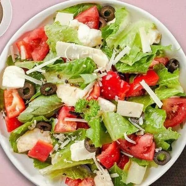 A vibrant salad with fresh lettuce, red tomatoes, black olives, and white cheese in a bowl.