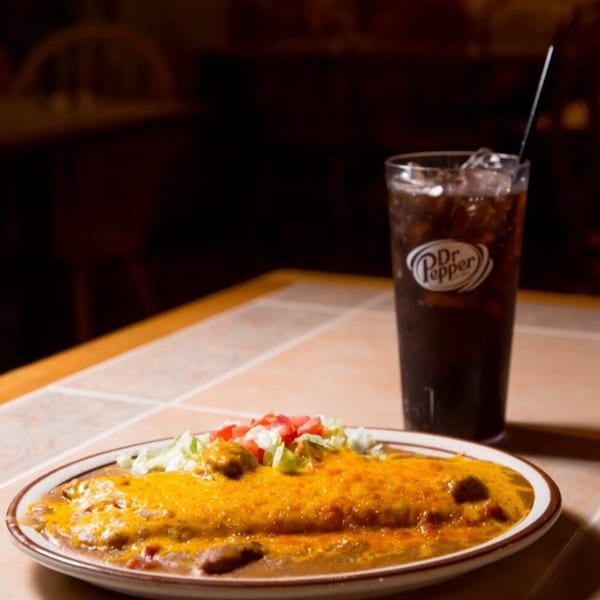 A plate of cheesy enchiladas with lettuce and tomato, next to a glass of Dr. Pepper.