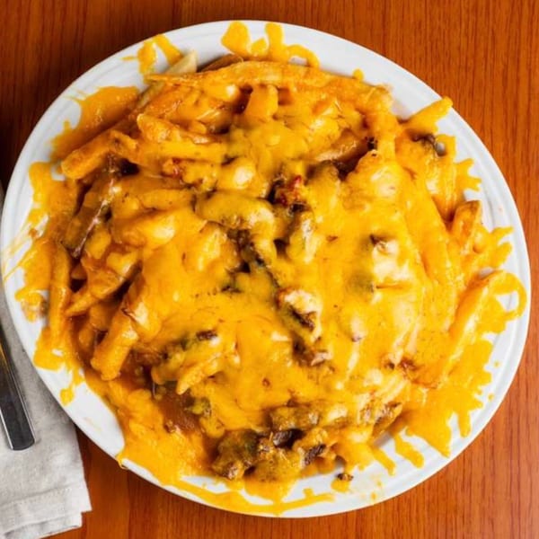 Moose Hill Cantina's cheesy fries, smothered in melted cheddar and bits of meat, on a white plate.